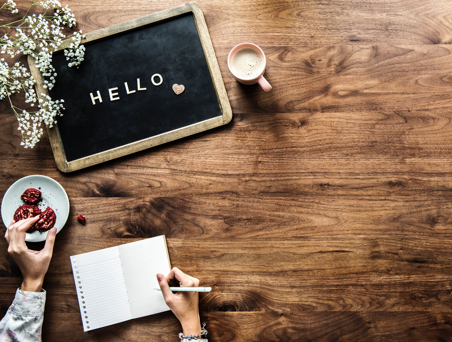 flat lay photography of person holding cookie and pen near hello board
